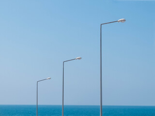 Three light poles opposite sea and blue sky. Minimalistic landscape with copy space