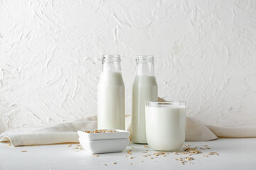 Bottles and glass of oat milk on light background