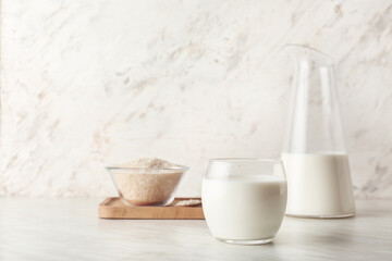 Jug and glass of rice milk on light background