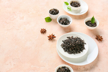 Bowls with dry black tea leaves on color background