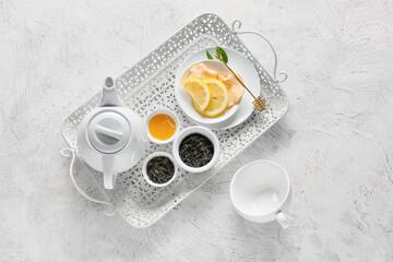 Teapot, bowls with dry black tea, lemon and honey on light background