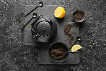Teapot, bowls with dry black tea and lemon on dark background