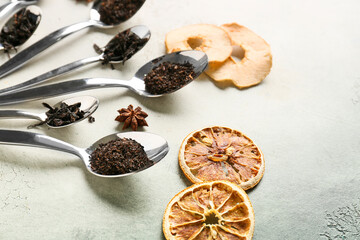 Spoons with dry black tea leaves and dried fruits on light background