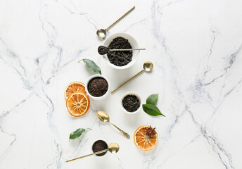 Bowls with dry black tea leaves, dried fruits and spoons on light background