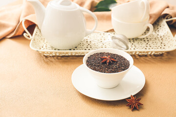 Teapot, bowl with dry black tea and anise on color background