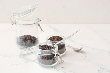 Jar with dry black tea and spoon on light background