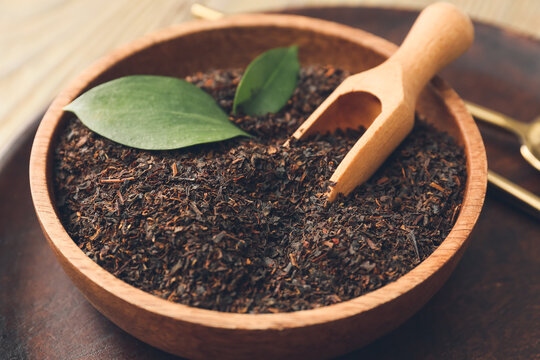 Bowl with dry black tea leaves and scoop on wooden background