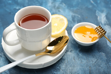 Cup of hot tea with honey and lemon on color background