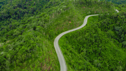 Top view of countryside road passing through the green forest and mountain in Thailand.