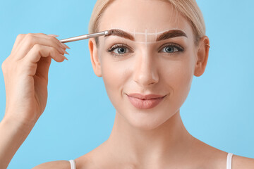 Young woman correcting her eyebrows on color background