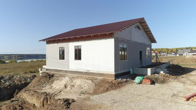 Drone view of façade of unfinished modern energy efficient house of foam blocks panels with roof with metal tile sheets. House in village. Sunny day
