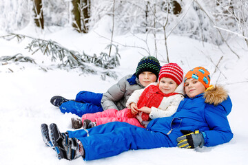 Two school kid boy and little toddler girl in winter forest. Happy children having fun with snow outdoors in winter. Family, three siblings, sister and brothers together, outdoors. Active leisure