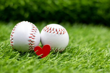 Baseballs are on green grass together with love red heart for Valentine's Day