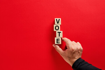 Male hand arranging the wooden blocks with the word vote on red background with copy space. Voting...