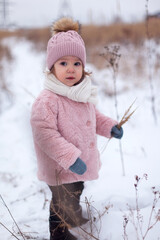 A little girl in a pink fur coat is having fun, playing outside, surrounded by snow. Winter time