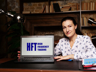 Woman showing laptop computer with  HFT HIGH FREQUENCY TRADING icon on screen background, success in business concept
