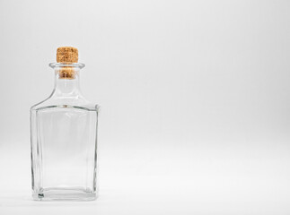 Empty glass bottle closed with cork cap isolated on a white background. Transparent square bottle. Front view of the vertical staying jar.