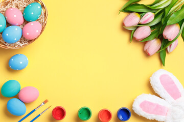 Naklejka na ściany i meble Happy easter. Multi-colored eggs in a basket, rabbit ears, tulips and paints on a yellow background. Flat lay greeting card. Copy space on medical protective mask.