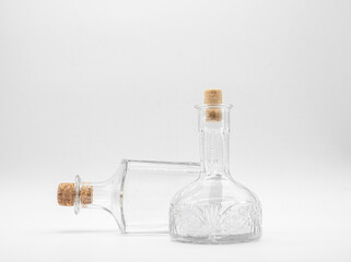 Upright empty glass carafe and empty glass bottle lying on its side closed with cork caps isolated on a white background. Pair of the transparent bottles with different shape.