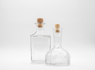 Empty glass carafe and empty glass bottle closed with cork caps isolated on a white background. Pair of the transparent bottles. Front view of the two vertical staying jars with different shape.