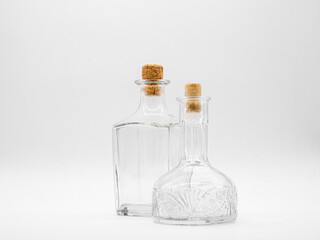 Empty glass carafe and empty glass bottle closed with cork caps isolated on a white background. Pair of the transparent bottles. Front view of the two vertical staying jars with different shape.