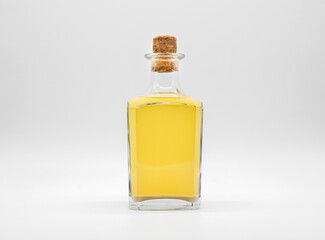 Glass bottle with alcohol drink closed with cork cap isolated on a white background. Transparent square bottle with yellow liquid. Front view of the vertical staying jar.
