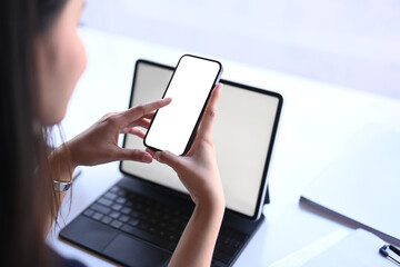 Close up view of young woman sitting in front of her tablet computer and using mobile phone.