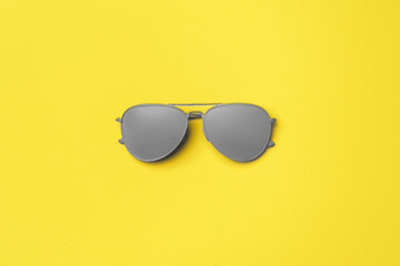 Gray painted sunglasses on yellow background top view