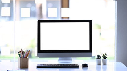 Front view of modern computer, stationery and plant on white table. White empty screen for advertise text.