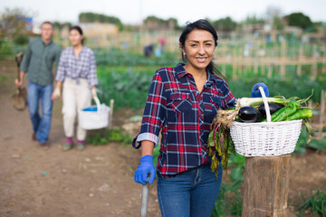 Portrait of happy hispanic woman showing rich crop of vegetables in kitchen garden on sunny fall day
