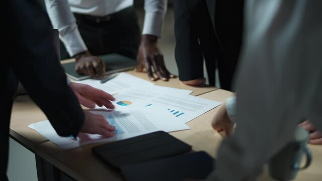 Business meeting, international management team at work, team is standing next to a work table and works with documents, discussing work plans and planning financial statistics, brainstorm, view of