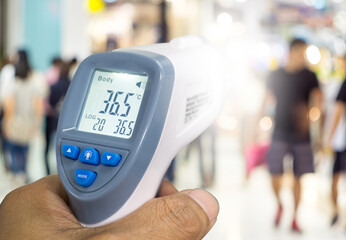 Hand holding infrared thermometer to measuring temperature on blurred Asian people walking past the Corona virus screening point, Covid 19.