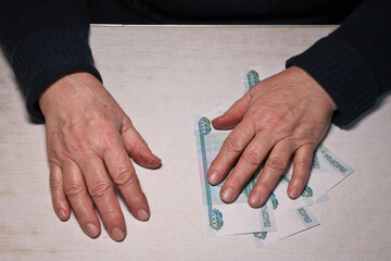 An elderly woman's hand lies on a bundle of thousand-ruble bills. Old woman's hands and money. Old age, retirement savings and investment concept.