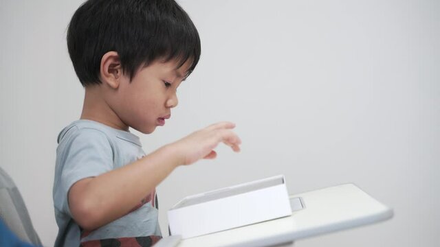 Asian boy about 4 years old using computer tablet in a box with happy smile as self study at home