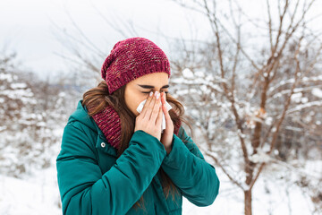 Young woman blowing in a tissue in a cold winter with a snowy mountain in the background. Portrait...