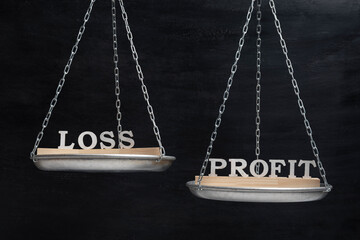 Words LOSS and PROFIT in balance. Scales on black background close up