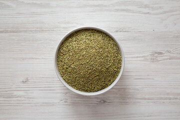 Organic Dried Rosemary in a Bowl on a white wooden background, overhead view. Flat lay, top view, from above.