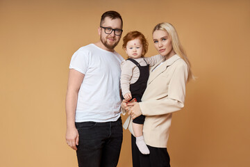 Happy family. Portrait of Mom, dad and daughter on a beige background. Beautiful couple in love holding their little daughter in their arms