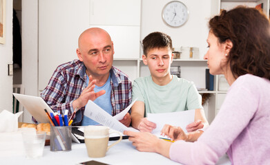 Parents with teenager son using laptop and analyzing their finances with documents at table