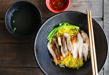 Roasted pork egg noodles in black bowl with soup and spicy dip on the side - Thai Chinese food called Bamee Moo Yang