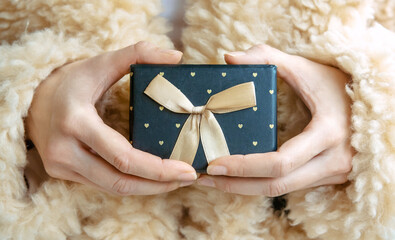 Female hands holding a small black gift box with bow 