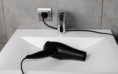 Hair dryer connected.
A black hair dryer for drying hair lies in the bathroom on a white washbasin.