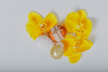 Easter eggs with yellow orchid flowers on white background. Happy Easter card. Easter eggs with lace border, wooden cutting board, brush on white table. Golden Easter egg.