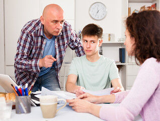Parents with teenager son reading and writing some documents at home table ..