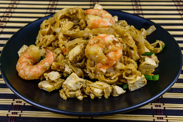 Black plate with pad thai on a bamboo mat