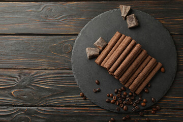 Tray with chocolate wafer rolls, coffee beans and chocolate on wooden background