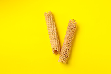 Tasty wafer rolls with condensed milk on yellow background