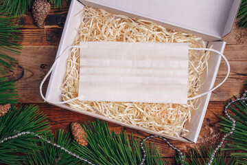 Safe Christmas, pandemic New Year 2021 present box concept. Covid-19. Pine branches, cones, beads, protective gauze mask on wooden background.