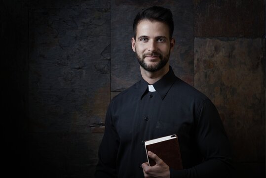 Portrait of handsome young priest with prayer book against dark background.