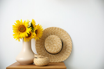 Fototapeta na wymiar Bouquet of beautiful sunflowers, wicker basket and hat on table indoors